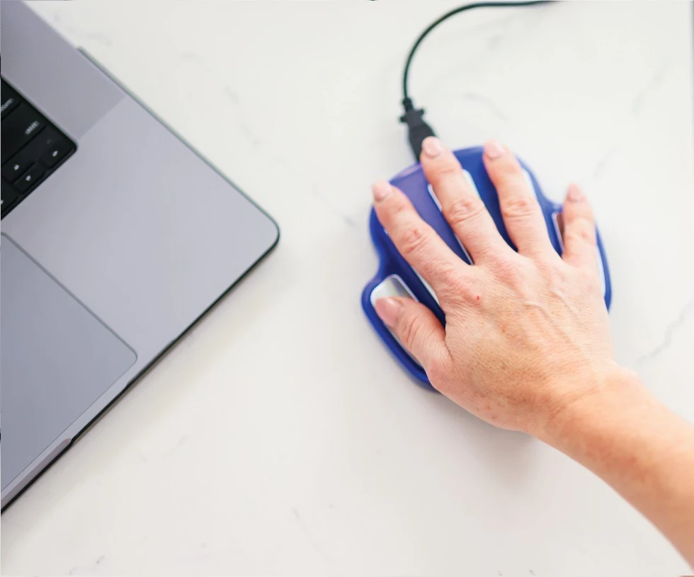 Hand resting on the authentic blue ZYTO Hand Cradle beside a laptop